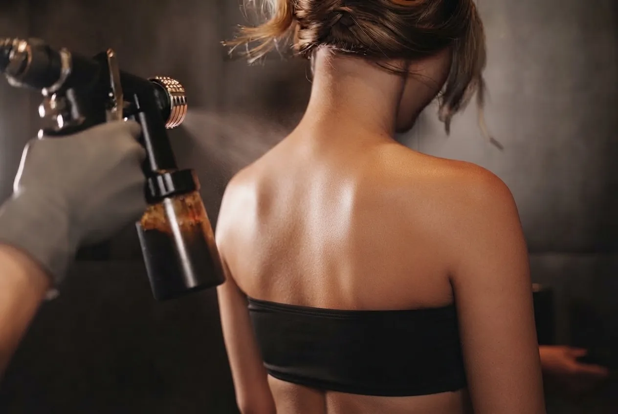 Airbrush misting tan across a client’s bare back